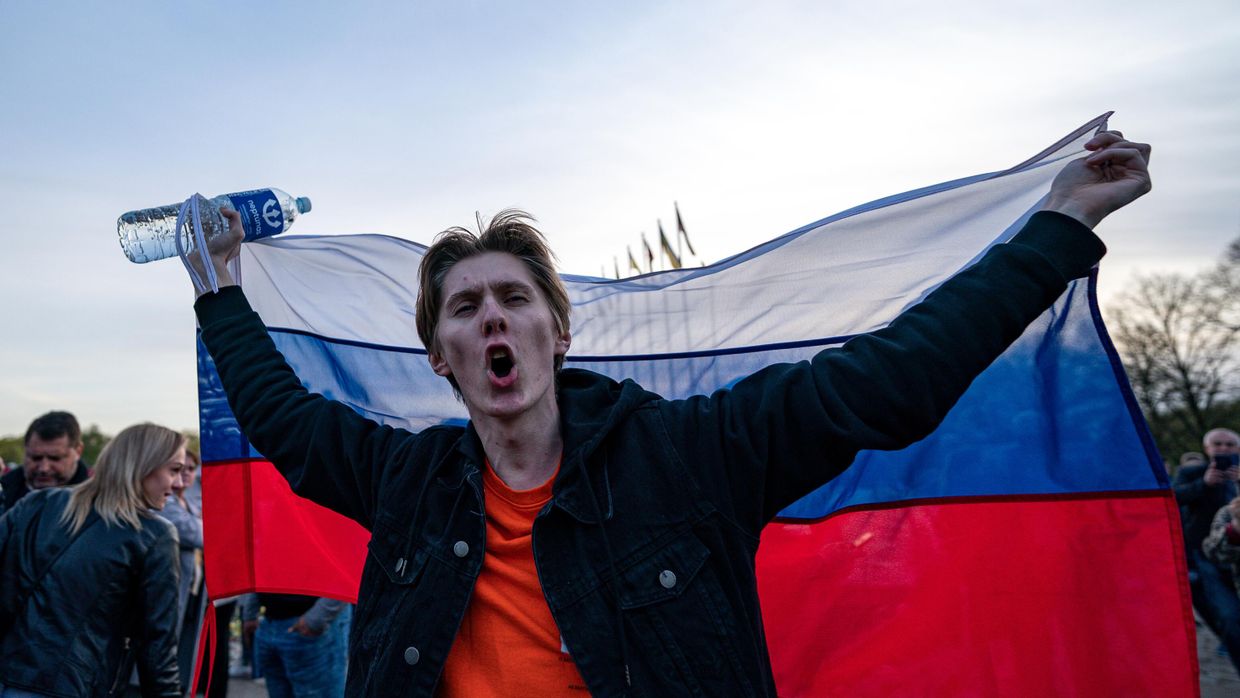 Молодой человек с российским флагом на церемонии возложения цветов у мемориального комплекса в Риге