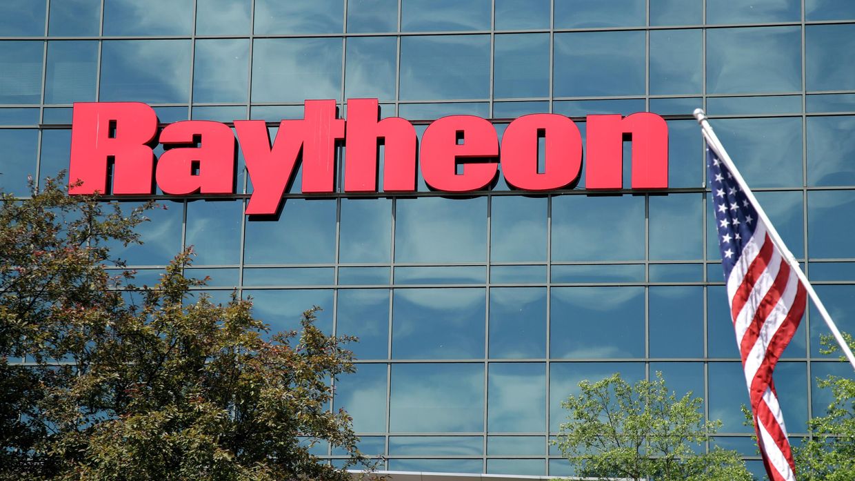 Флаг США на фоне вывески военно-промышленной компании Raytheon