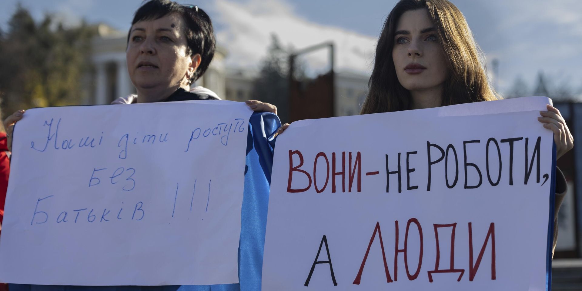 Мария Харченко, справа, которая ждет возвращения своего мужа с передовой, держит плакат с надписью Они не роботы, а люди во время митинга на площади Независимости в Киеве, 27 октября 2023 года. - ИноСМИ, 1920, 25.03.2024