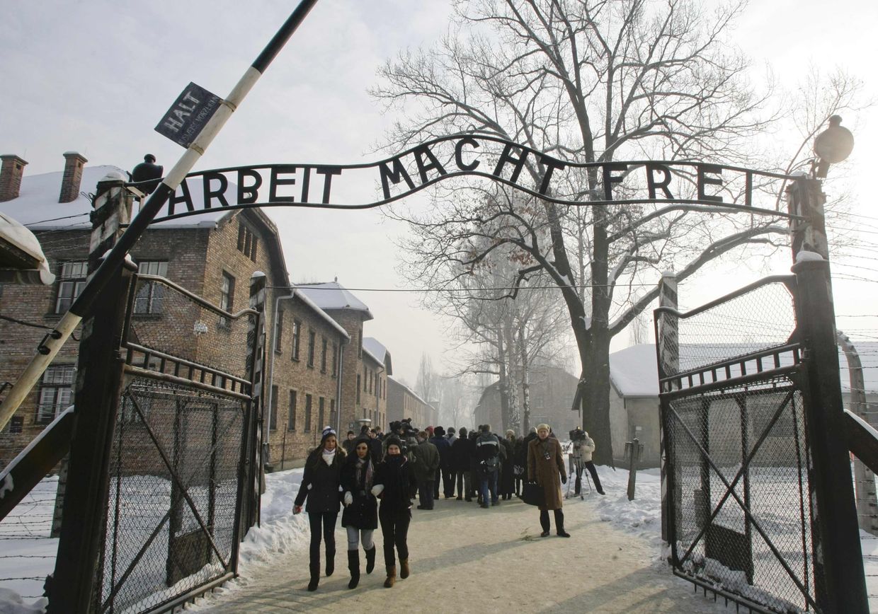 Люди ходят через ворота, с надписью Arbeit Macht Frei (работа освободит вас, бесплатно), бывшего нацистского лагеря смерти Аушвиц в Освенциме Люди ходят через ворота, с надписью Arbeit Macht Frei (работа освободит вас, бесплатно), бывшего нацистского лагеря смерти Аушвиц в Освенциме