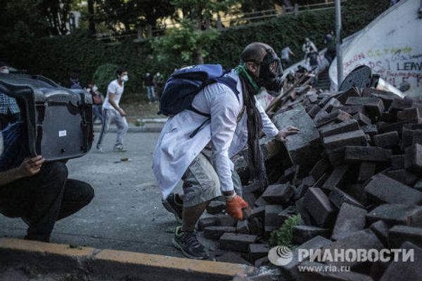 Один из протестующих прячется за баррикадой во время столкновения с сотрудниками полиции в Стамбуле