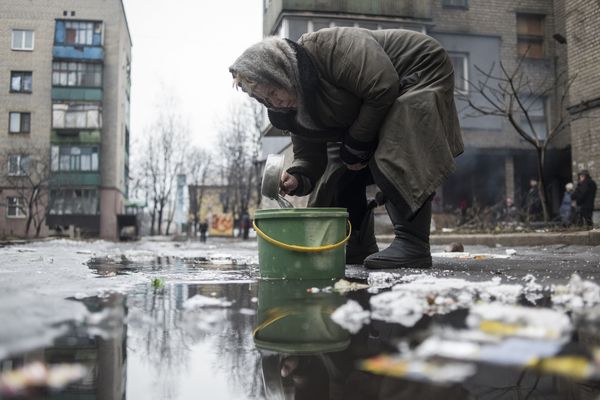 Пожилая жительница Дебальцево набирает воду из лужи