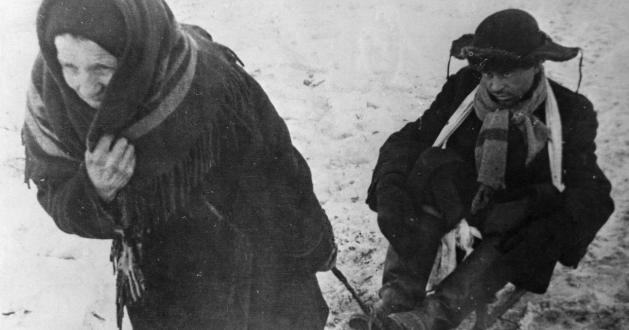 Жители блокадного Ленинграда: женщина везет ослабевшего от голода мужа на санках