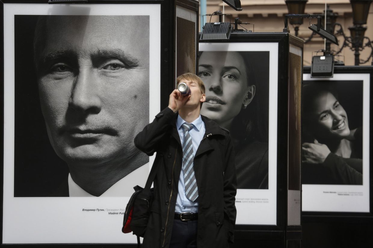 Мужчина пьет напиток на фоне фотографий Владимира Путина и российских спортсменов