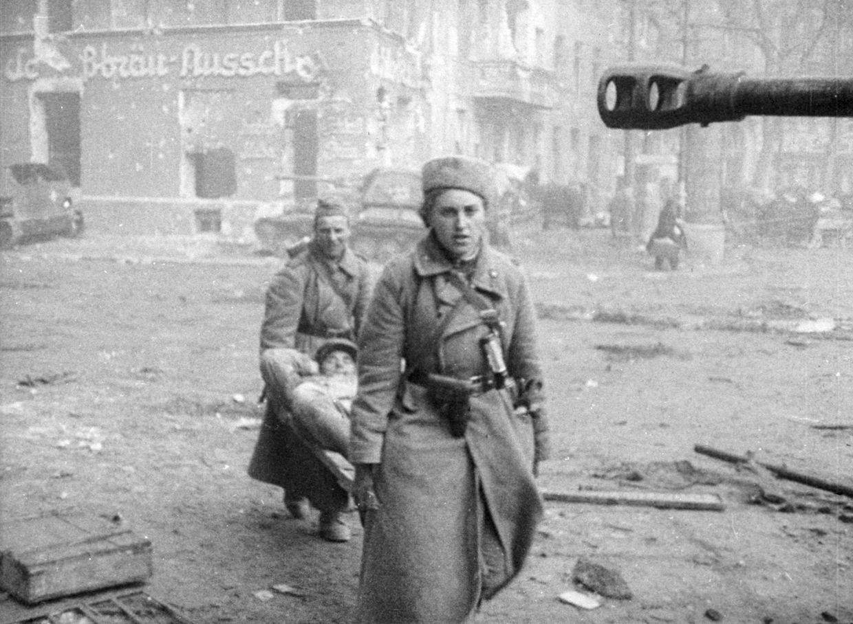 Женщина-санинструктор и санитар выносят на носилках раненого бойца