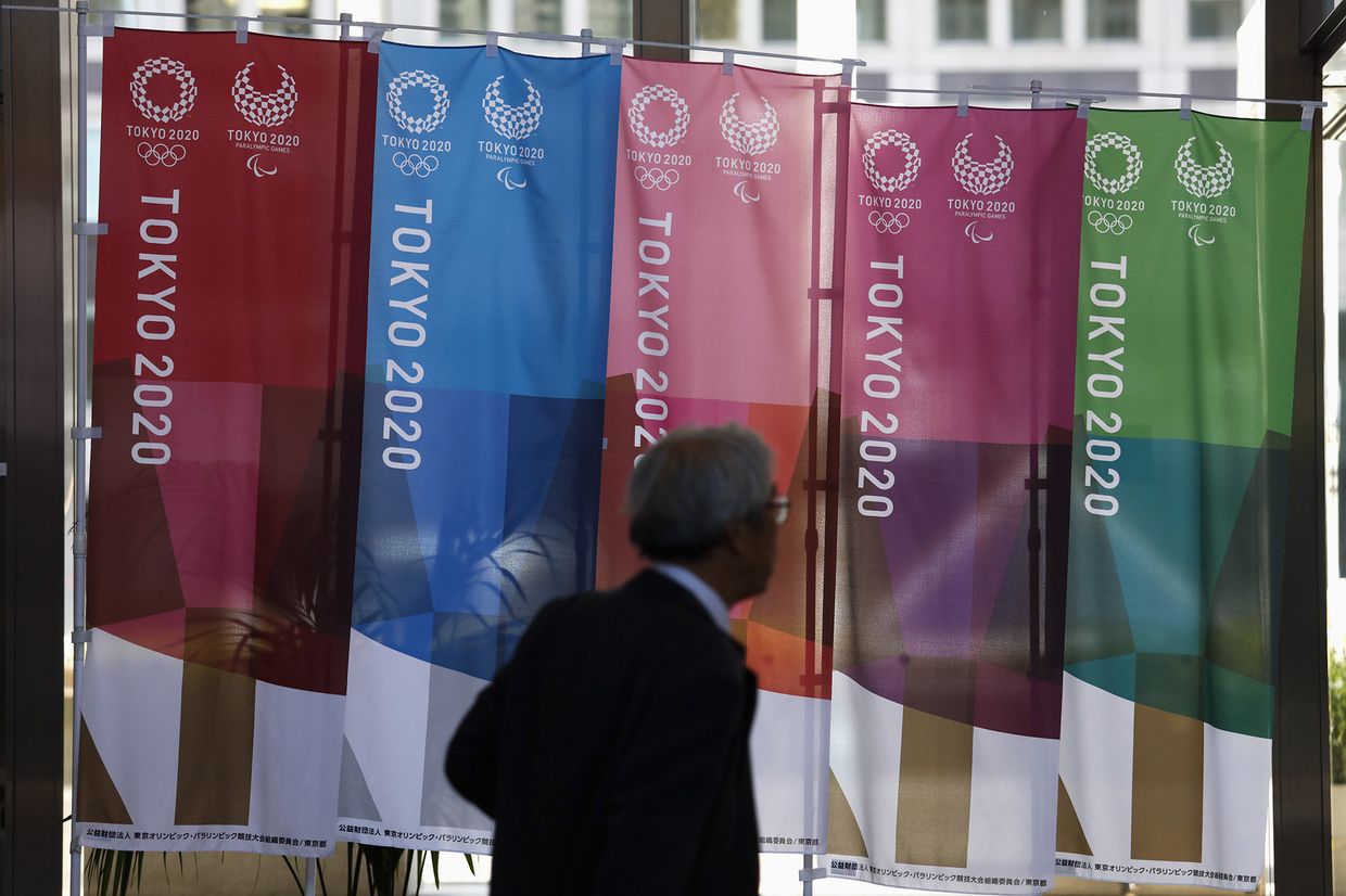 Мужчина проходит мимо баннеров Tokyo 2020