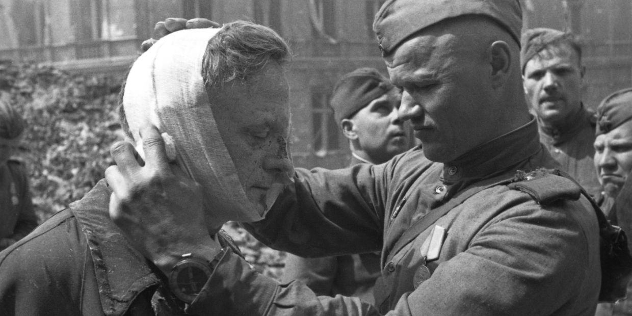 Великая Отечественная война 1941-1945 гг. Взятие Берлина Красной Армией. Советский солдат оказывает медицинскую помощь раненому местному жителю.